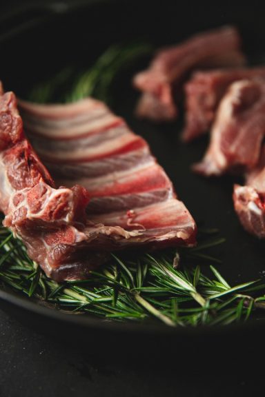 Rohes Fleischstück mit frischen Rosmarinnadeln auf einem schwarzen Teller.