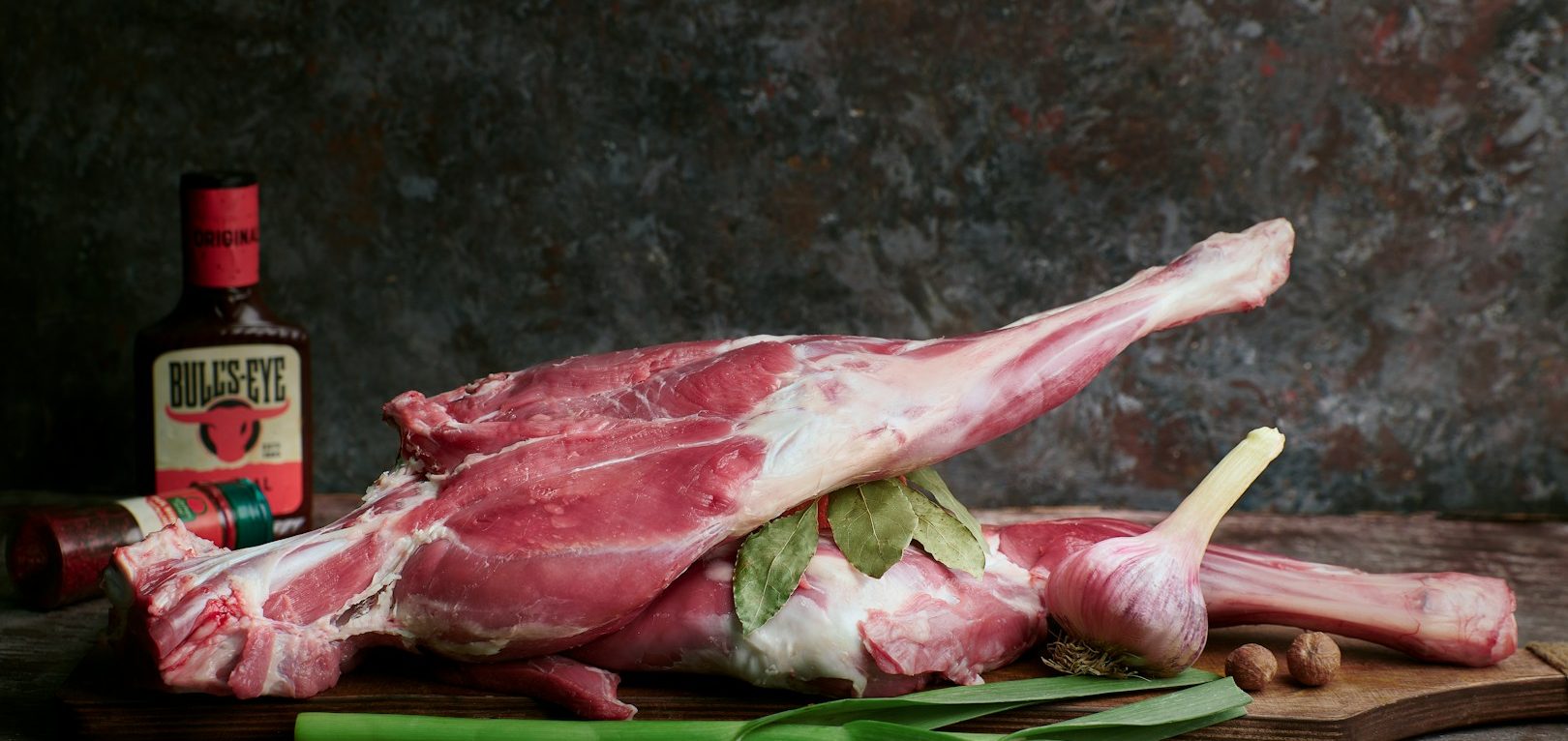 Rohe Lambshaxen auf einem Tisch, umgeben von Kräutern und einer Flasche Sojasauce.