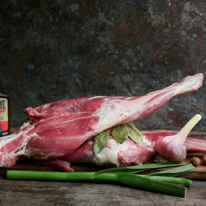 Rohes Lammhaxe mit Lauch und Gewürzen auf einem Holzbrett.