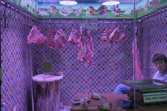 Fleischstücke hängen in einem stilisierten Verkaufsraum mit lila Beleuchtung.